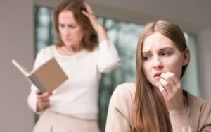 Worried teenager with mother in background reading, trying to figure out what to do