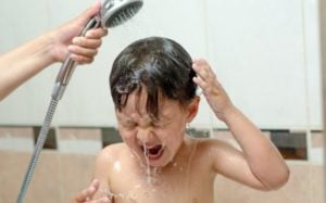 3 year old boy in bath tub getting his hair washed from detached sprayer. Mother trying to drown lice.