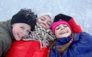 3 kids dressed in snow suits in the winter laying on skating rink